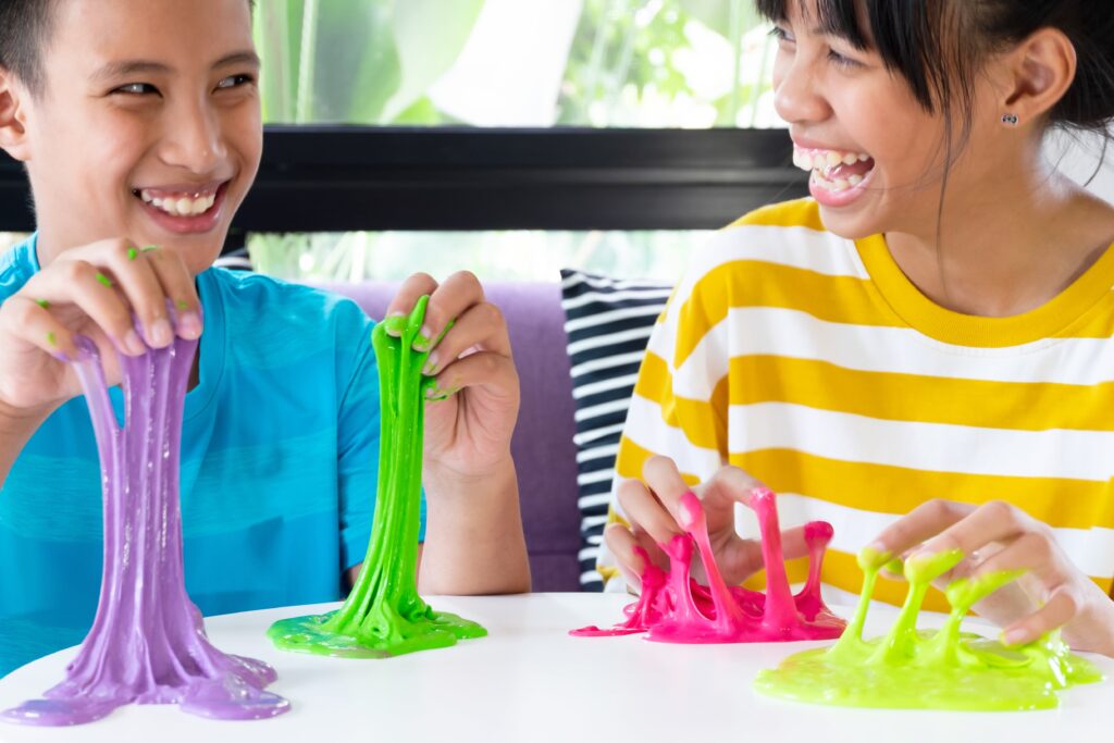 Hand Holding Homemade Toy Called Slime, Sibling boy and girl having fun and being creative by science experiment.